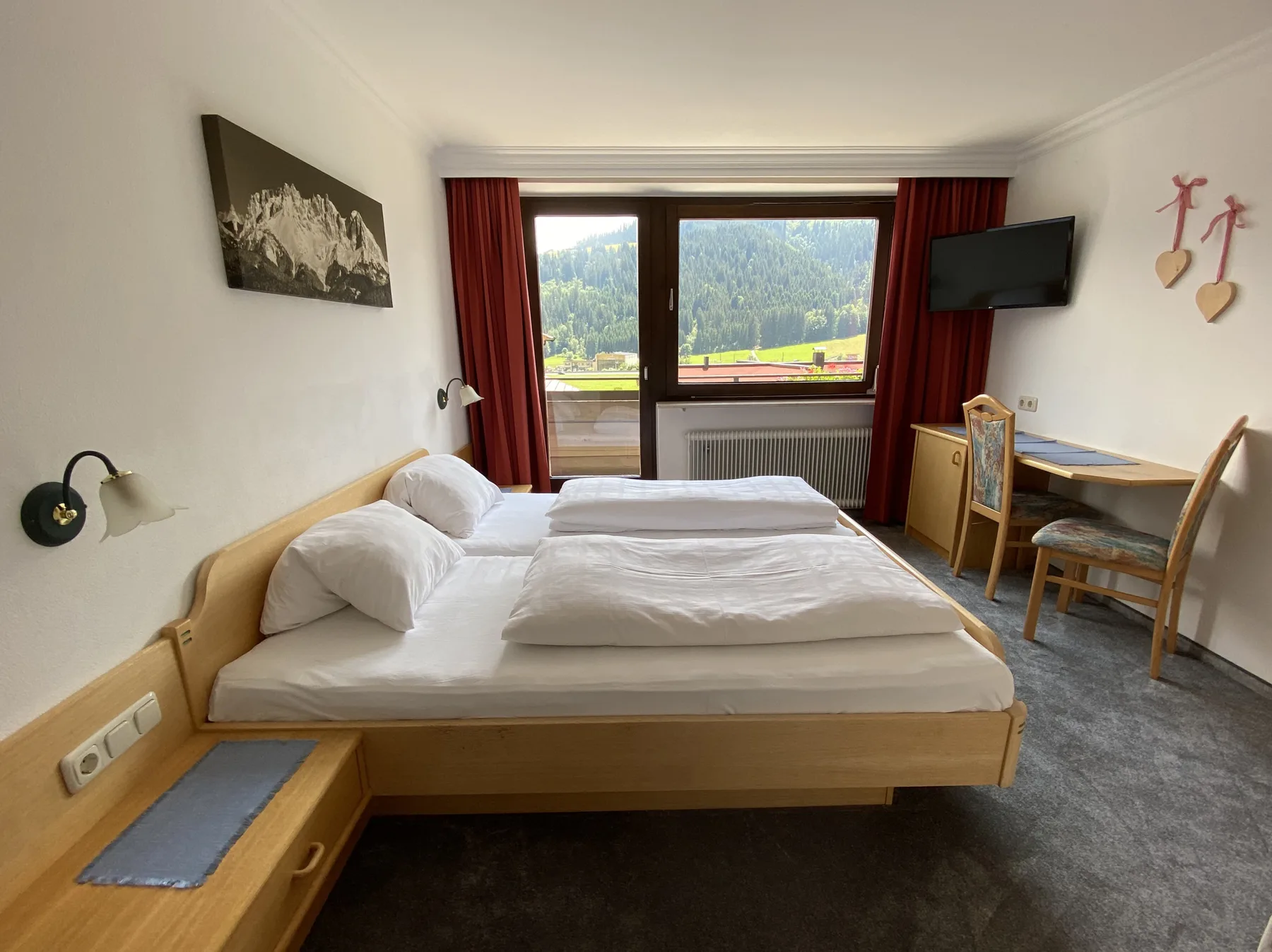 Dormitorio con una cama de madera, escritorio y una gran ventana con vistas a colinas verdes.