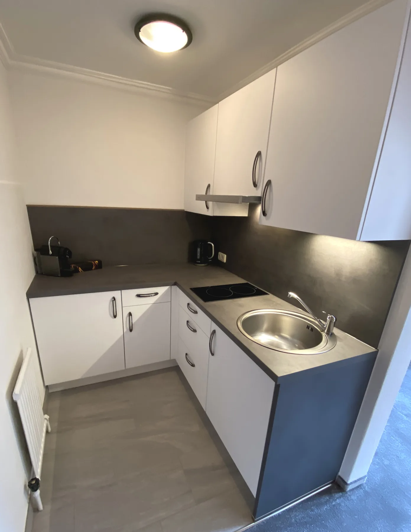 Una cocina compacta con armarios blancos, encimeras oscuras, una placa de cocina y un fregadero.