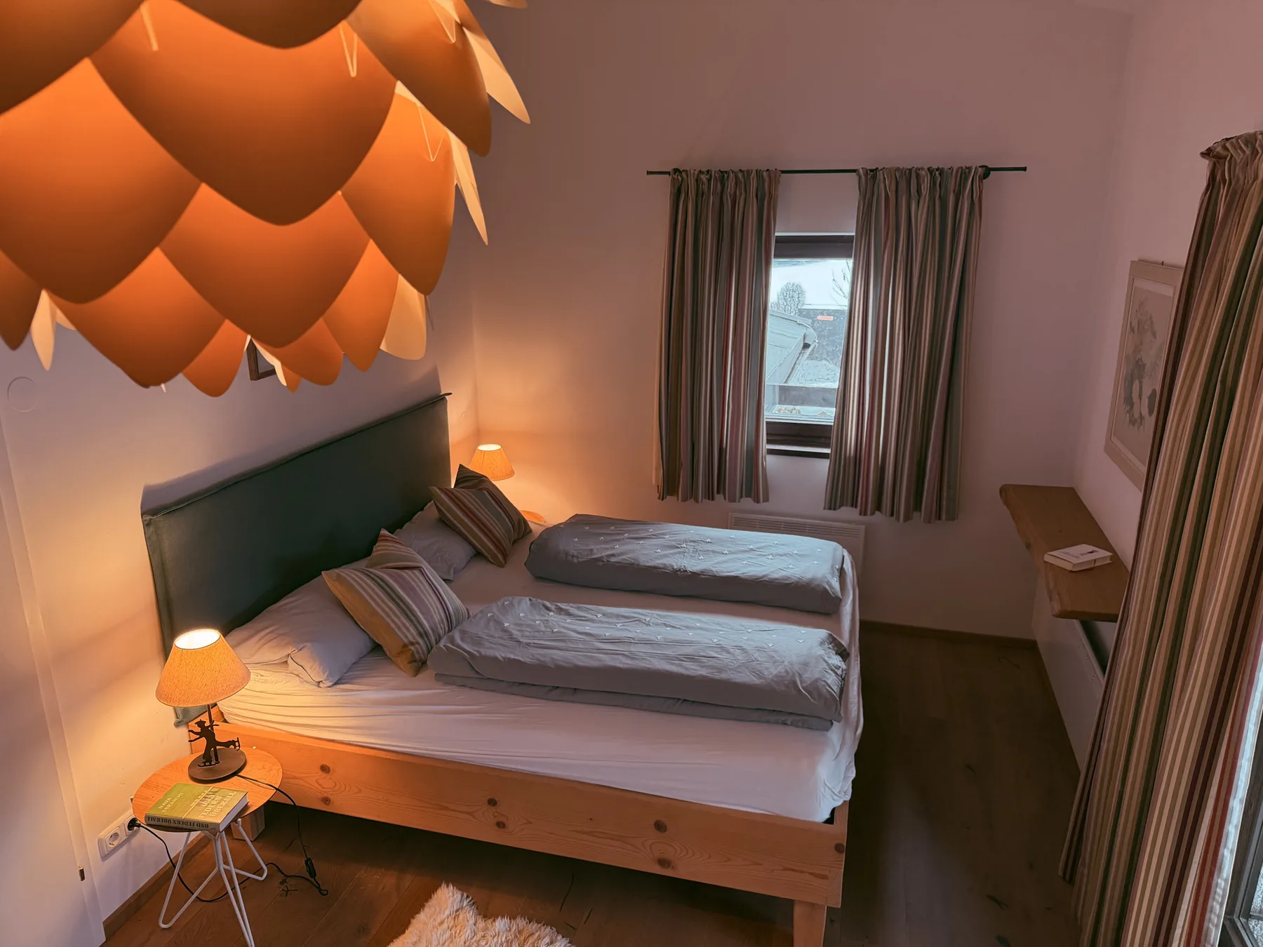 A bedroom with a bed beneath a warm orange pendant light.