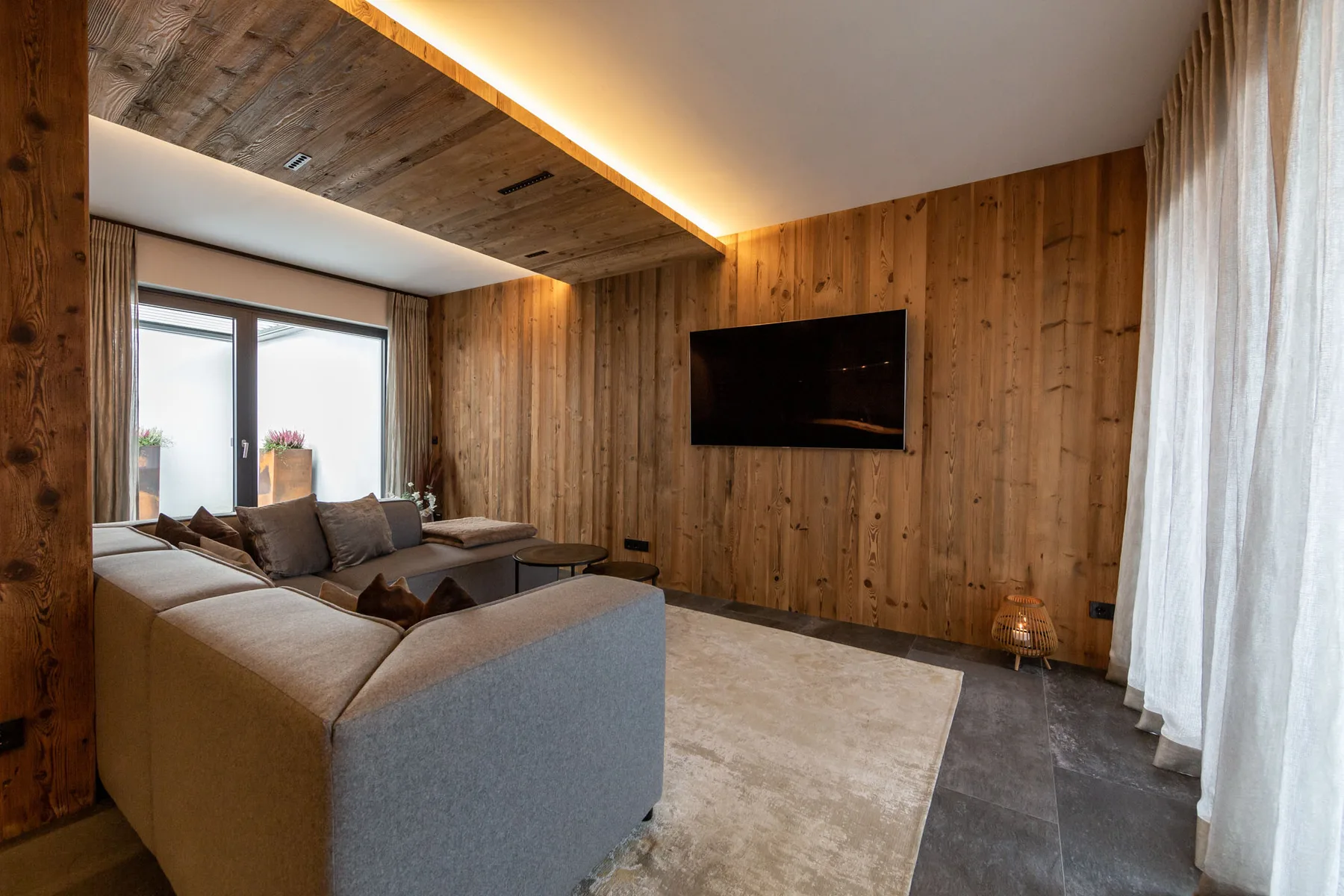 A living room with seating, a television, and large windows.