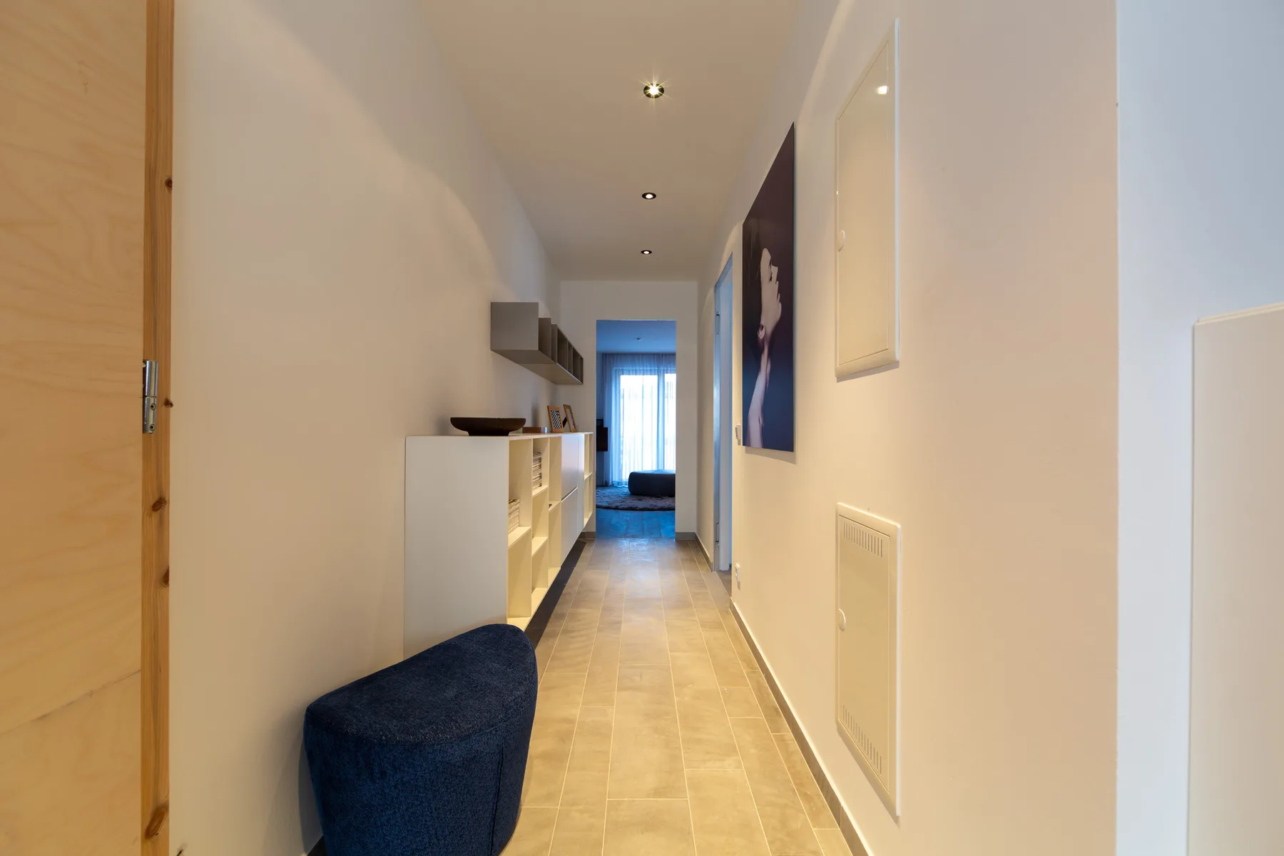 A narrow hallway with tiled flooring, a console, and a blue upholstered bench.
