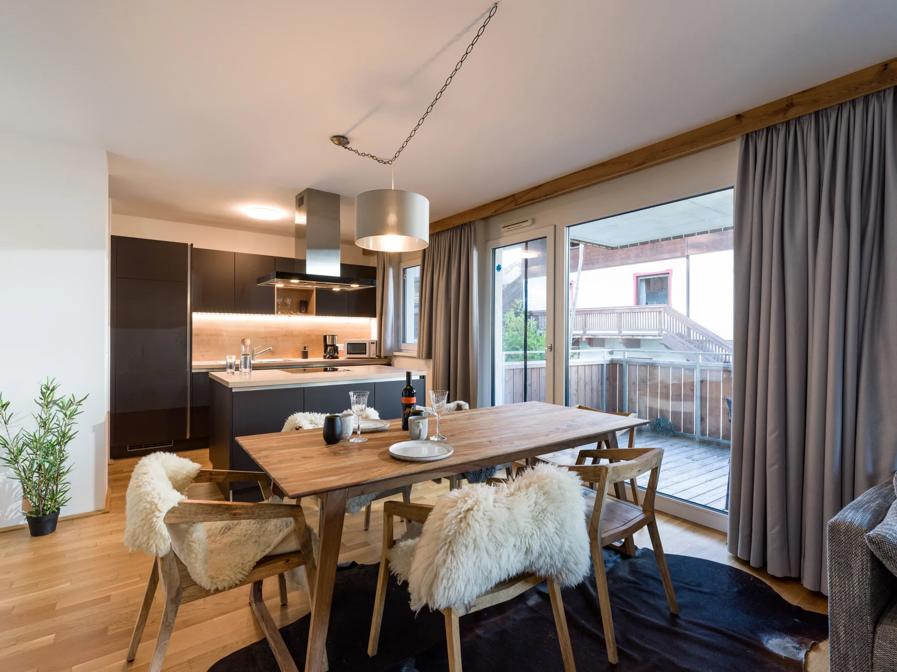 Comedor con una mesa de madera junto a una cocina moderna y puertas de vidrio.