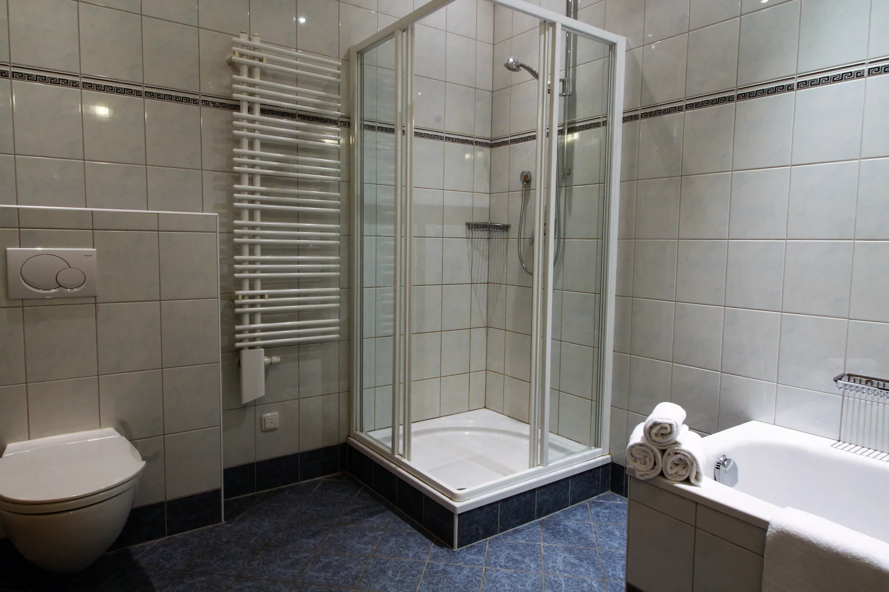 A tiled bathroom with a shower, bathtub, and wall-mounted towel warmer.