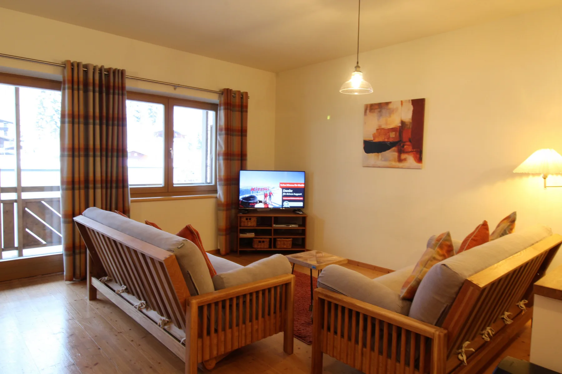 Living room with wooden seating, a television, and windows opening onto a balcony.