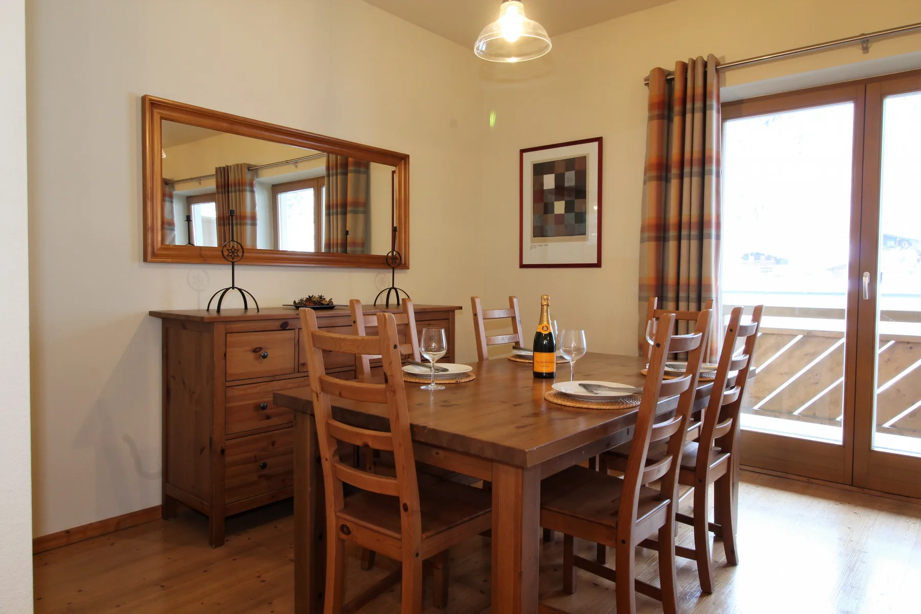 A wooden dining table and chairs sit beside glass doors opening onto a balcony.