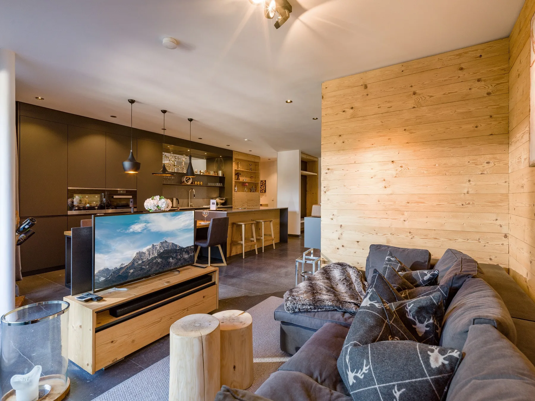Una sala de estar con un sofá frente a un televisor y una cocina abierta al fondo.