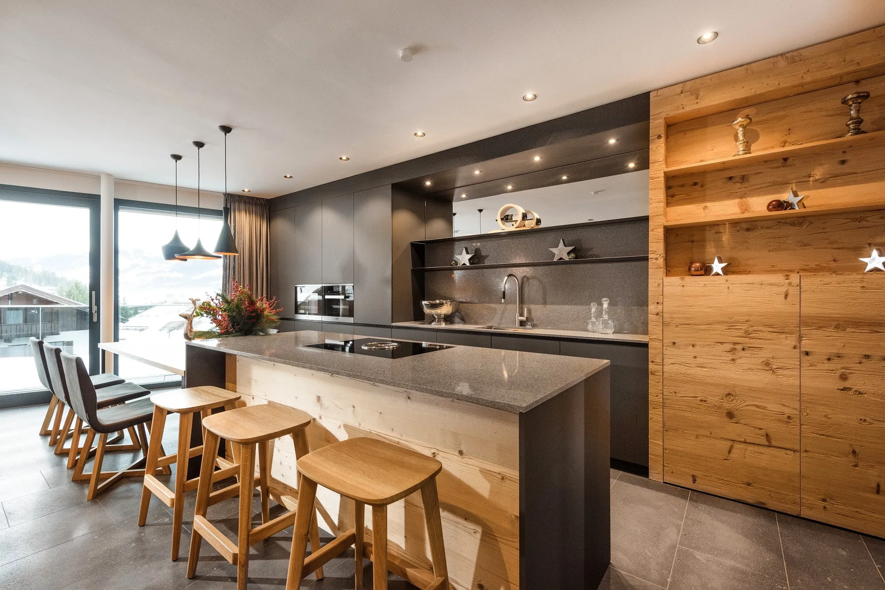 Una cocina moderna con una isla alargada, taburetes y grandes ventanas.
