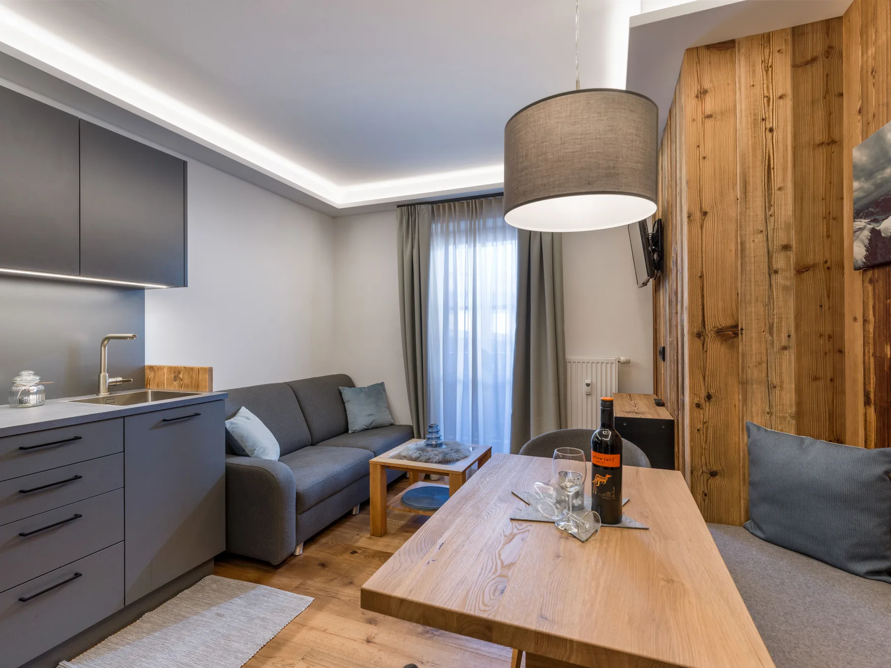 A modern living room with a kitchenette, seating, and a wooden dining table.