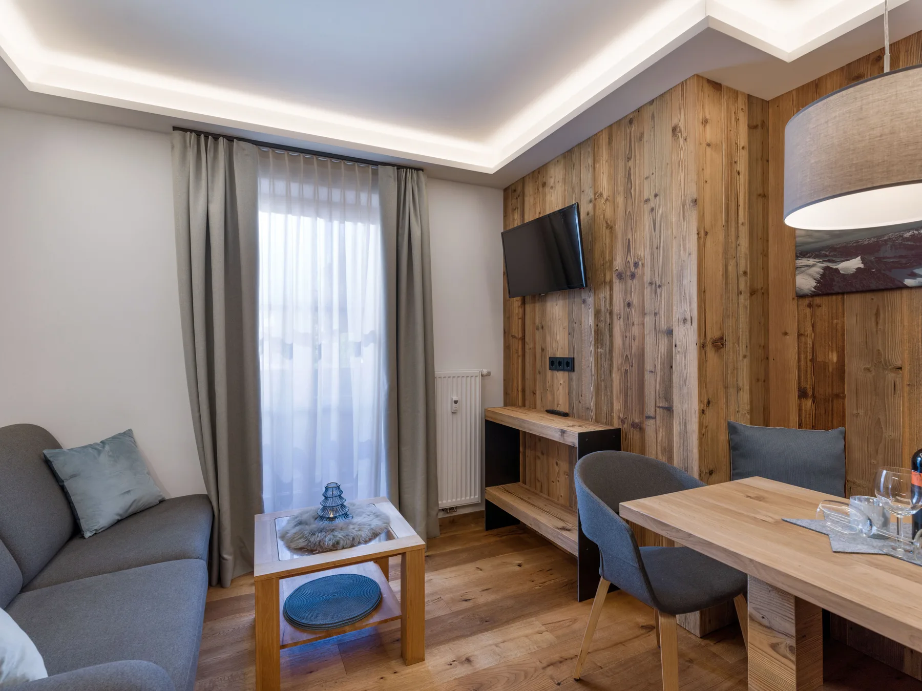 A living and dining area with seating, a wooden table, and a wall-mounted television.