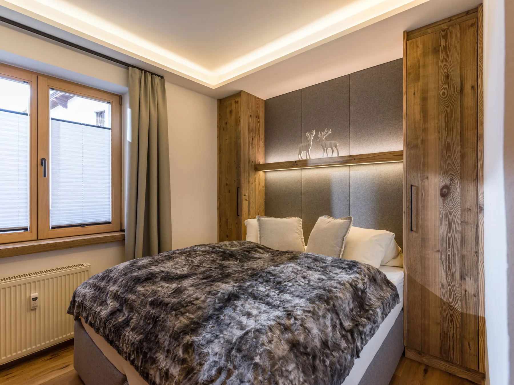 A bedroom with a bed beneath a padded wall panel and wood accents.