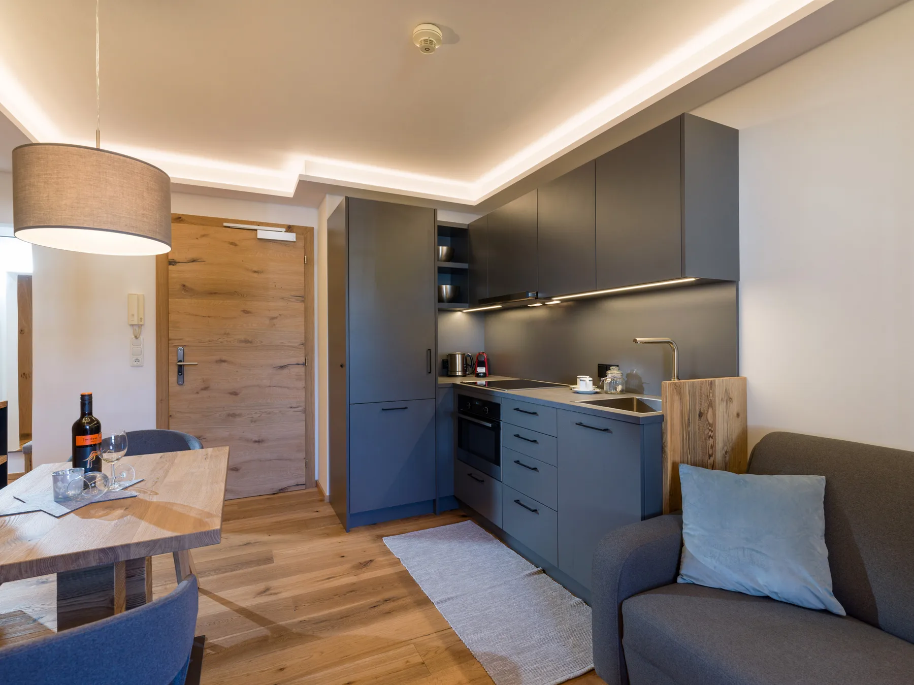 A modern kitchen and seating area with dark cabinets and a wooden entry door.