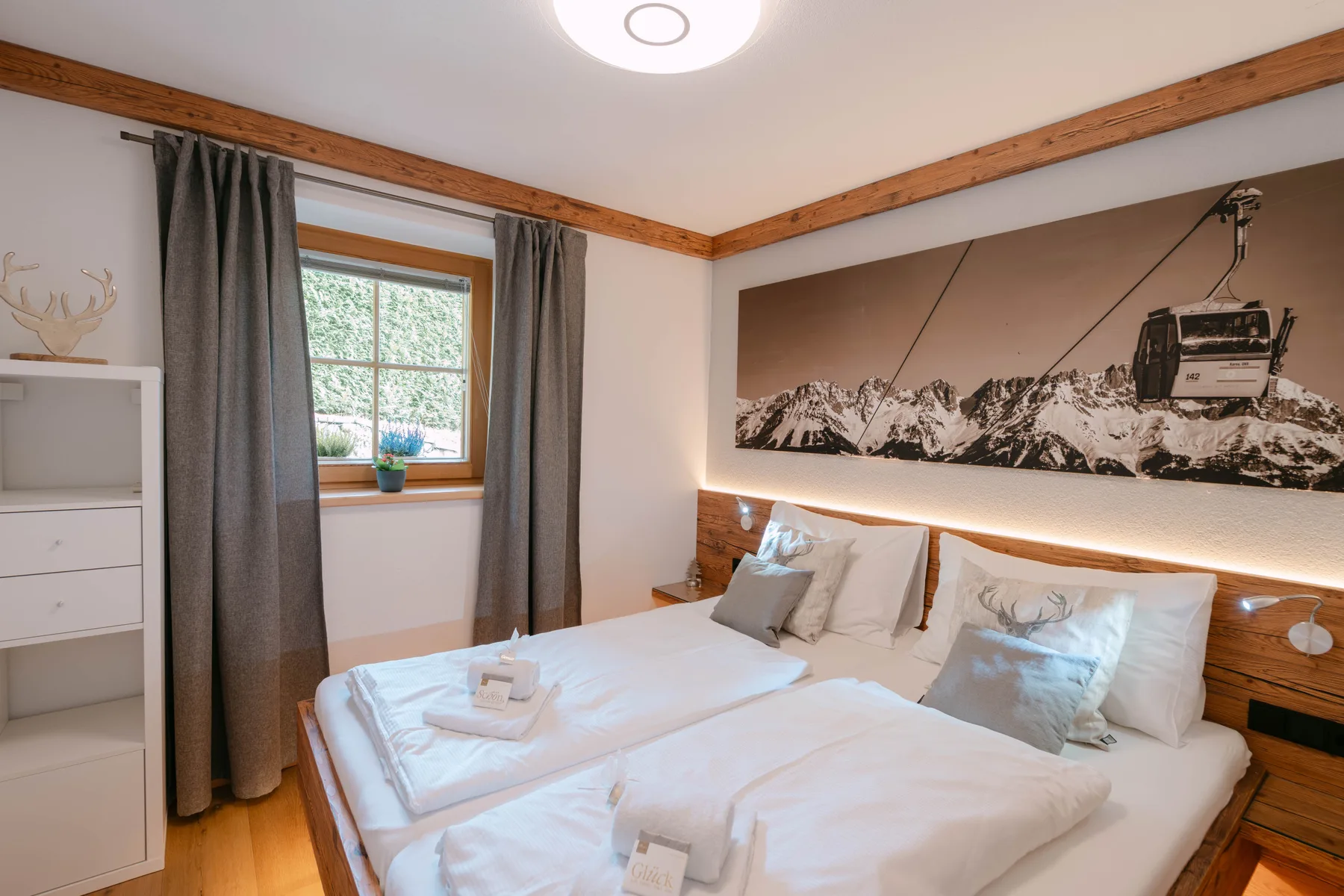 A bedroom with two beds, gray curtains, and a mountain mural above the headboard.
