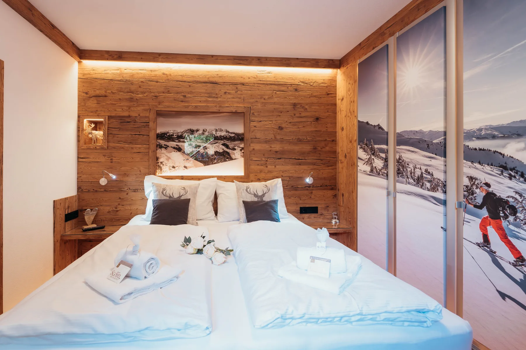 A bedroom with a neatly made bed and large windows overlooking a snowy mountain landscape.