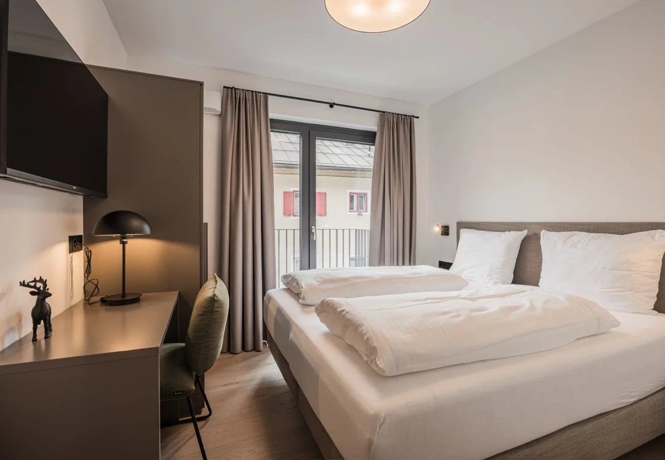 Un dormitorio con una cama grande junto a un escritorio y puertas de balcón.