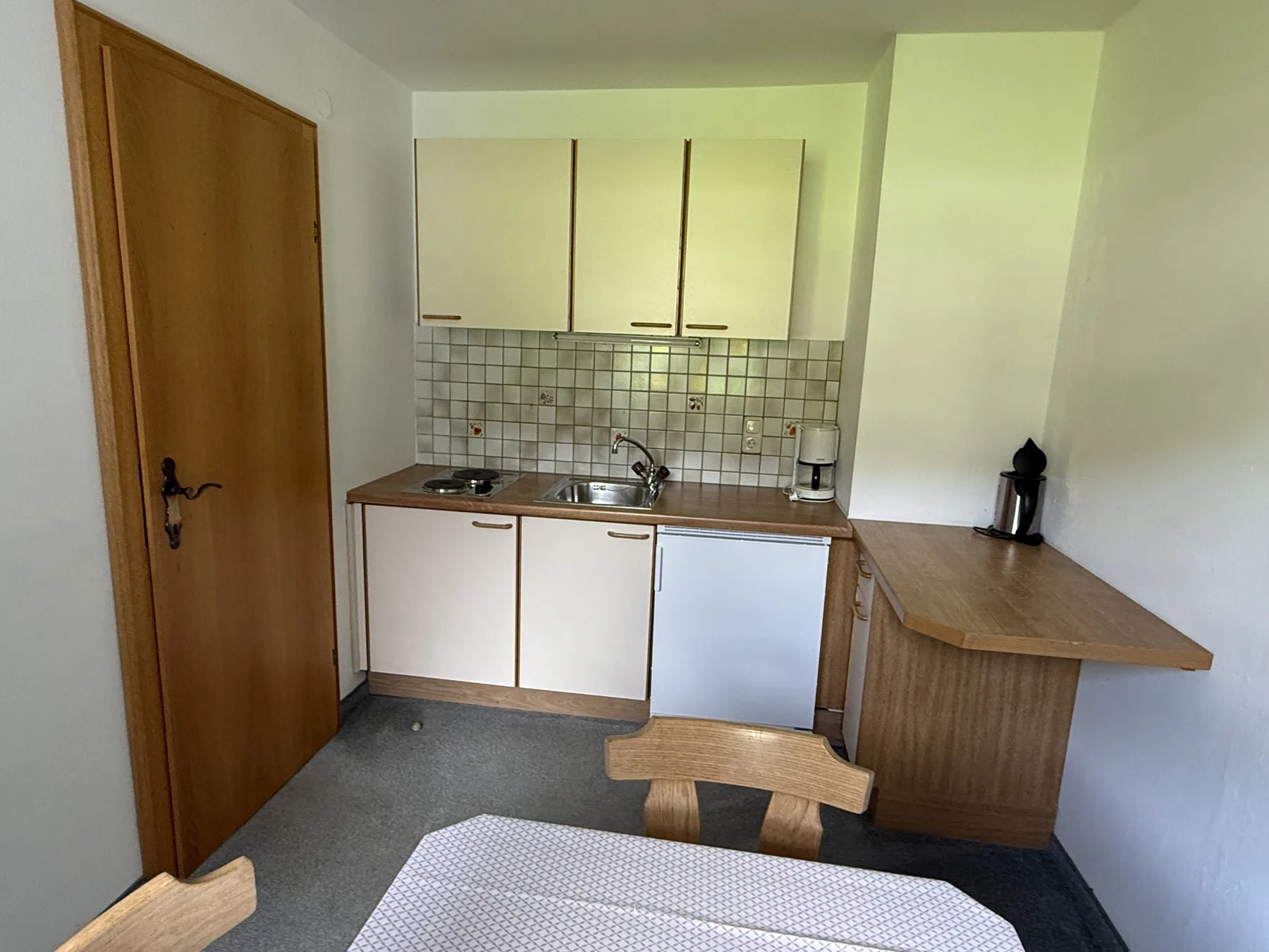 Una cocina compacta con gabinetes blancos, un salpicadero de azulejos y una encimera de madera.