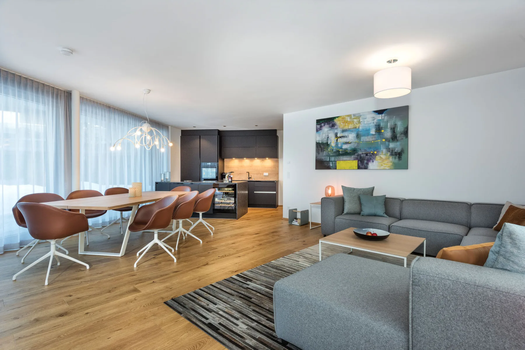 Un espacio diáfano de sala y comedor con un sofá seccional gris y una mesa de comedor de madera.