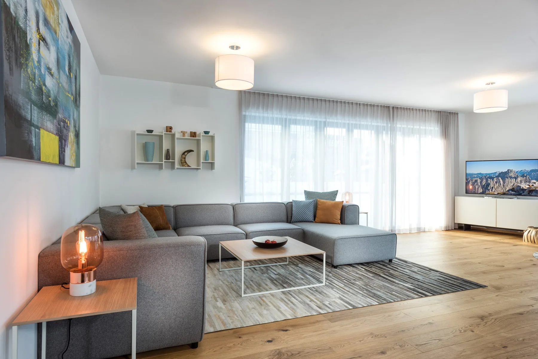 A bright living room with gray seating, a coffee table, and large curtained windows.