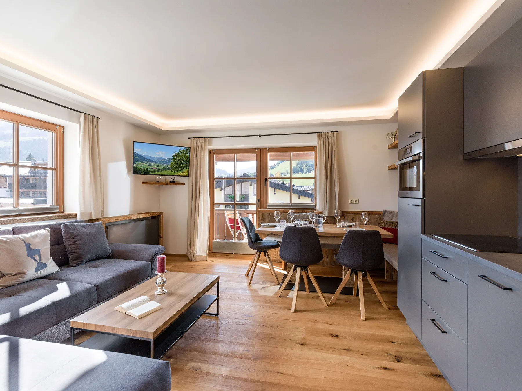Sala de estar con zona de descanso, mesa de comedor y ventanas con vistas a las montañas.