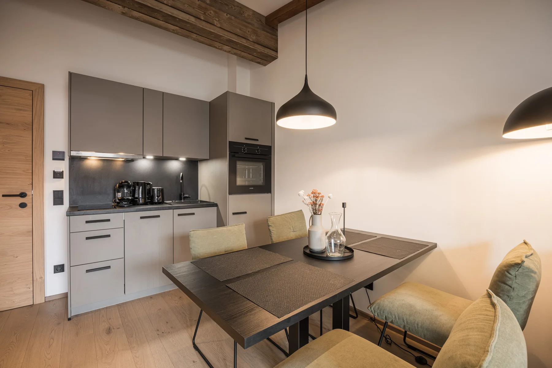 A modern kitchen and dining area with a table, seating, and pendant lights.