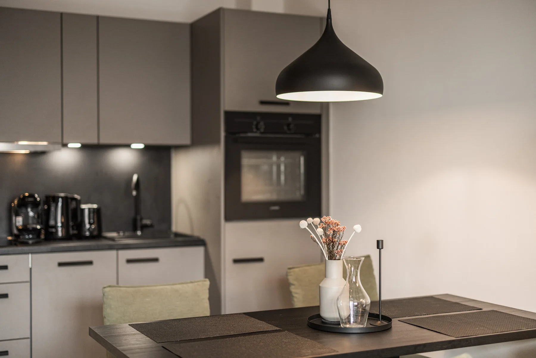 A modern kitchen with a dark island and pendant light.