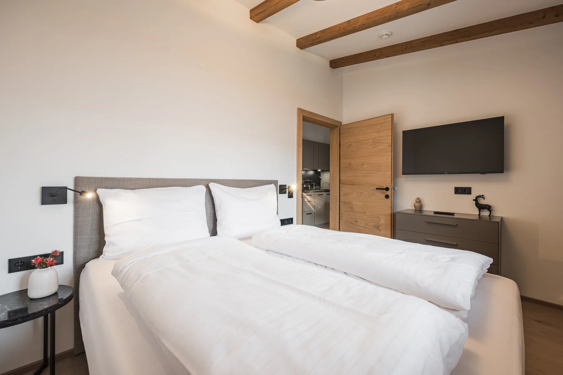 A bedroom with a neatly made bed and a wall-mounted television.
