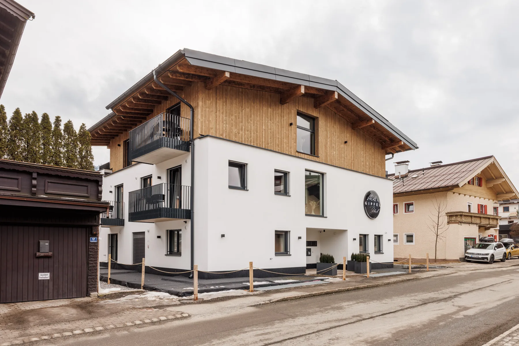 A modern multi-story building with white walls and a timber upper level beside a road.