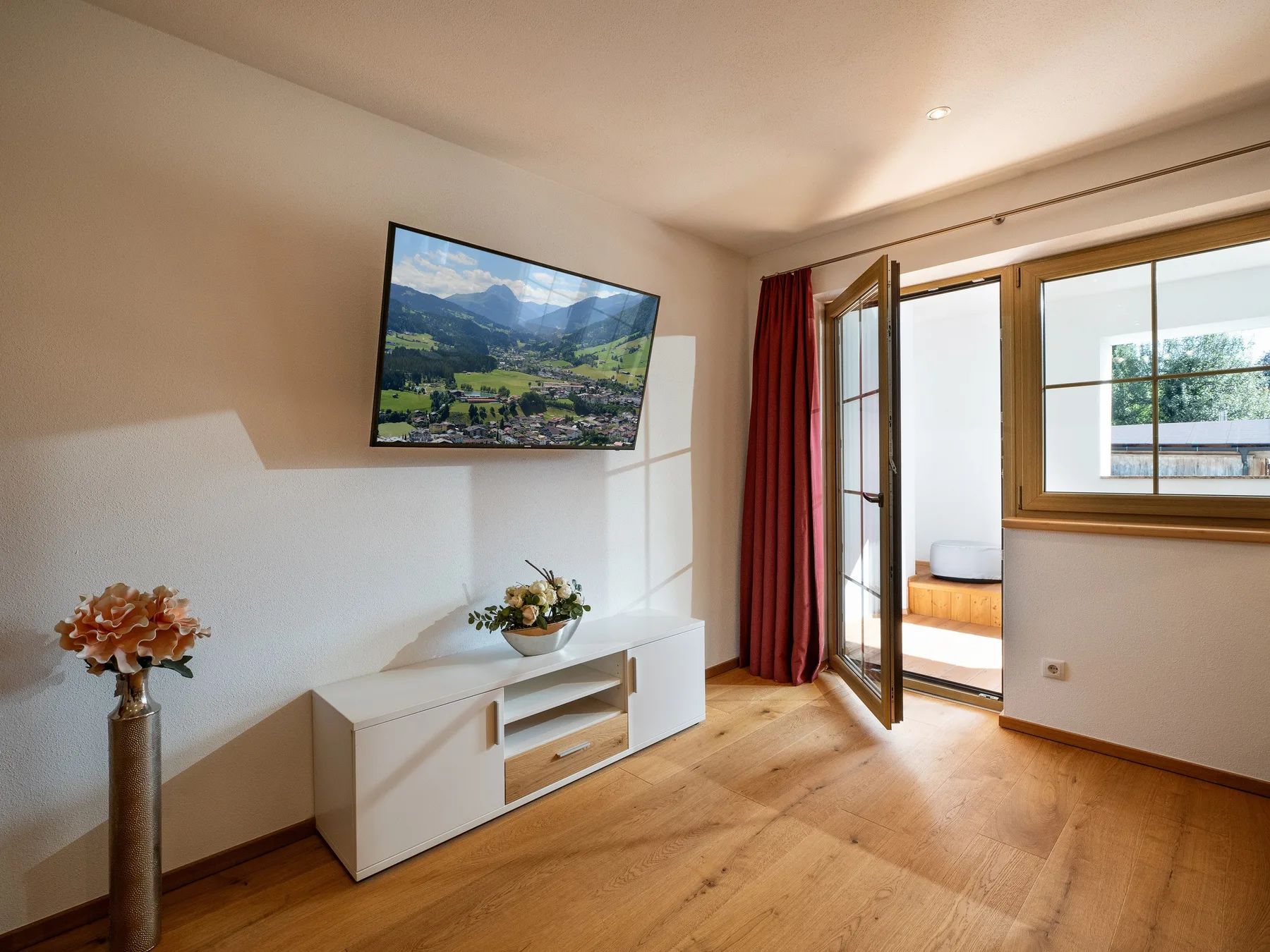 Sala de estar con televisor, mueble bajo y puerta abierta al balcón.