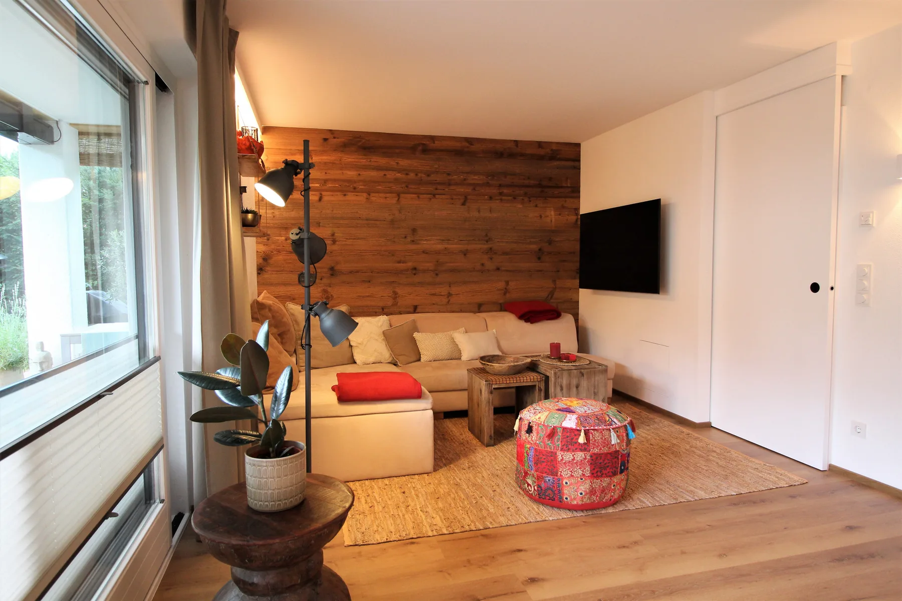 A living room with seating, a low table, and a television on the wall.