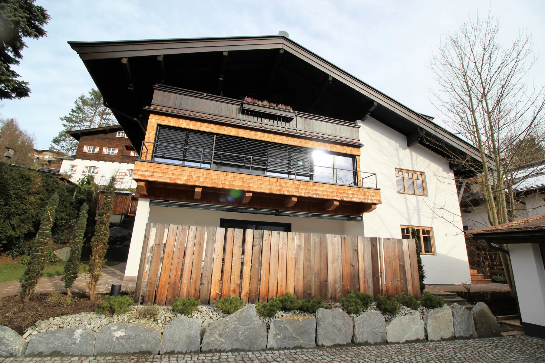 A multi-story building with wooden balconies stands beside a stone retaining wall.