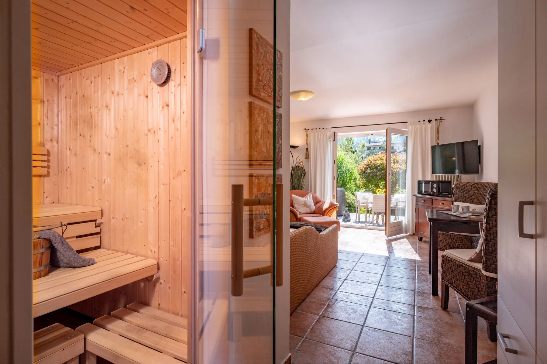 A living area with a visible sauna beside it and a glass door opening to a balcony.