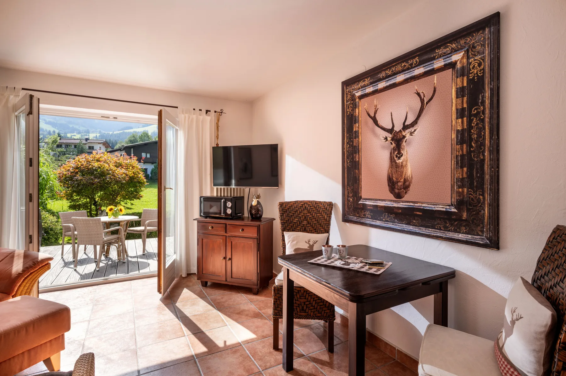A bright living area with a dining table, television, and an open patio door.