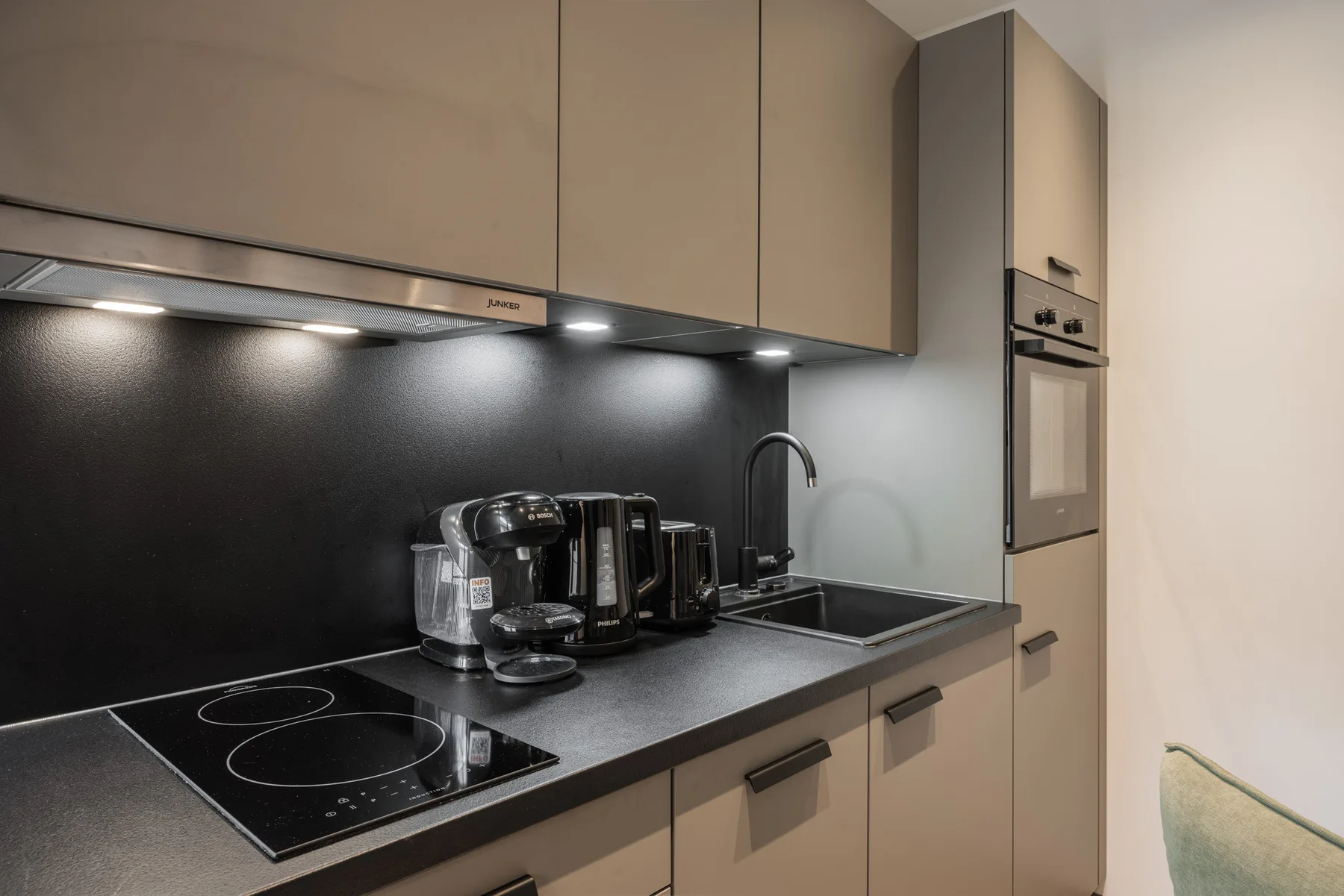 A modern kitchen with dark countertops, a cooktop, and built-in appliances.