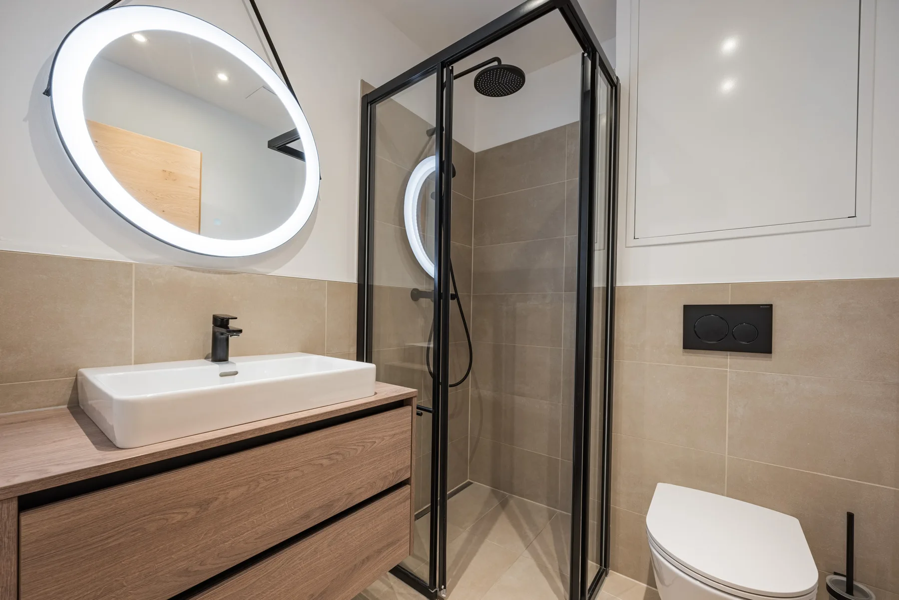 Un baño moderno con lavabo, espejo iluminado y ducha de vidrio.