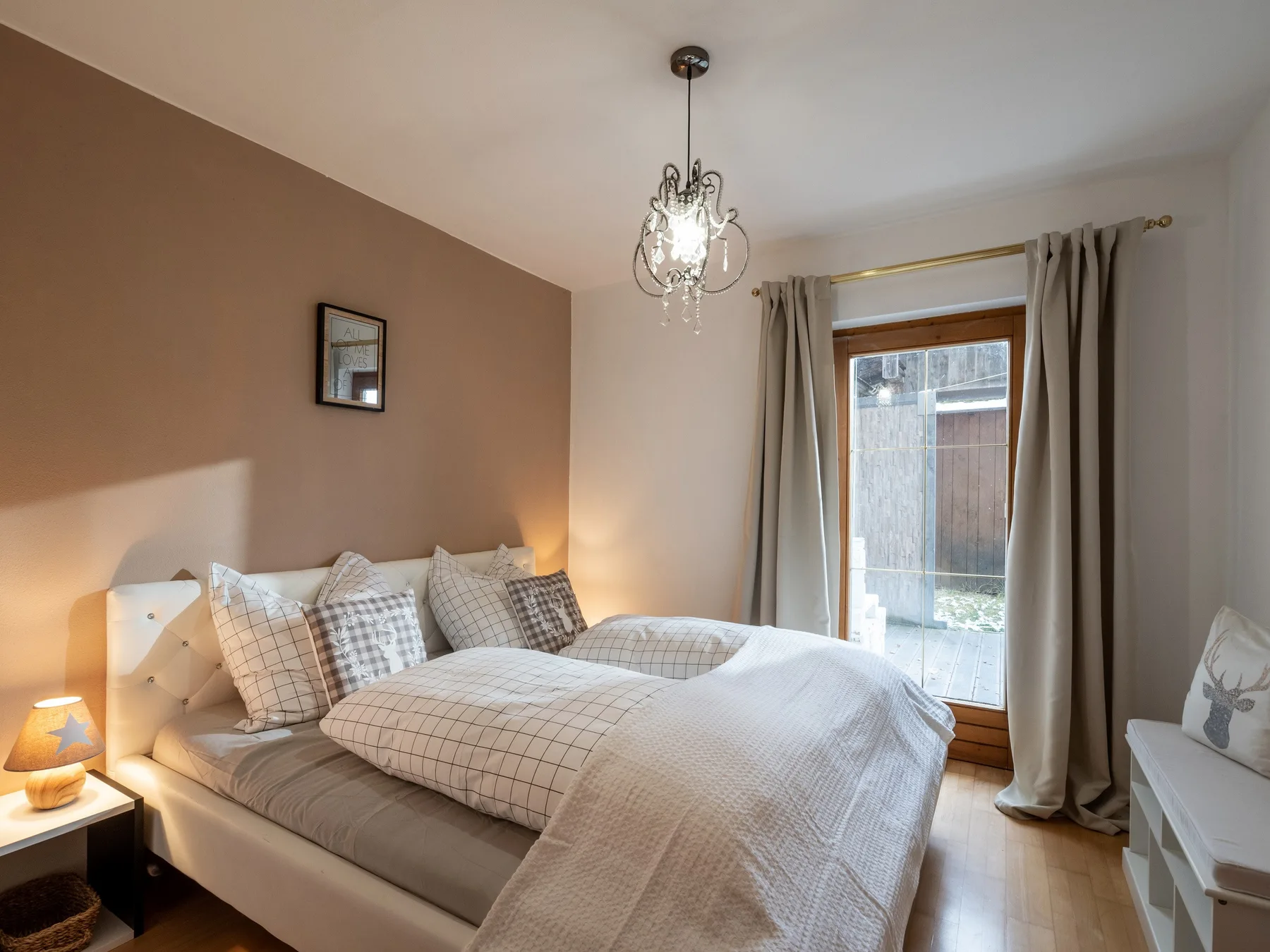 Un dormitorio con una cama bien hecha junto a una ventana alta con cortinas.