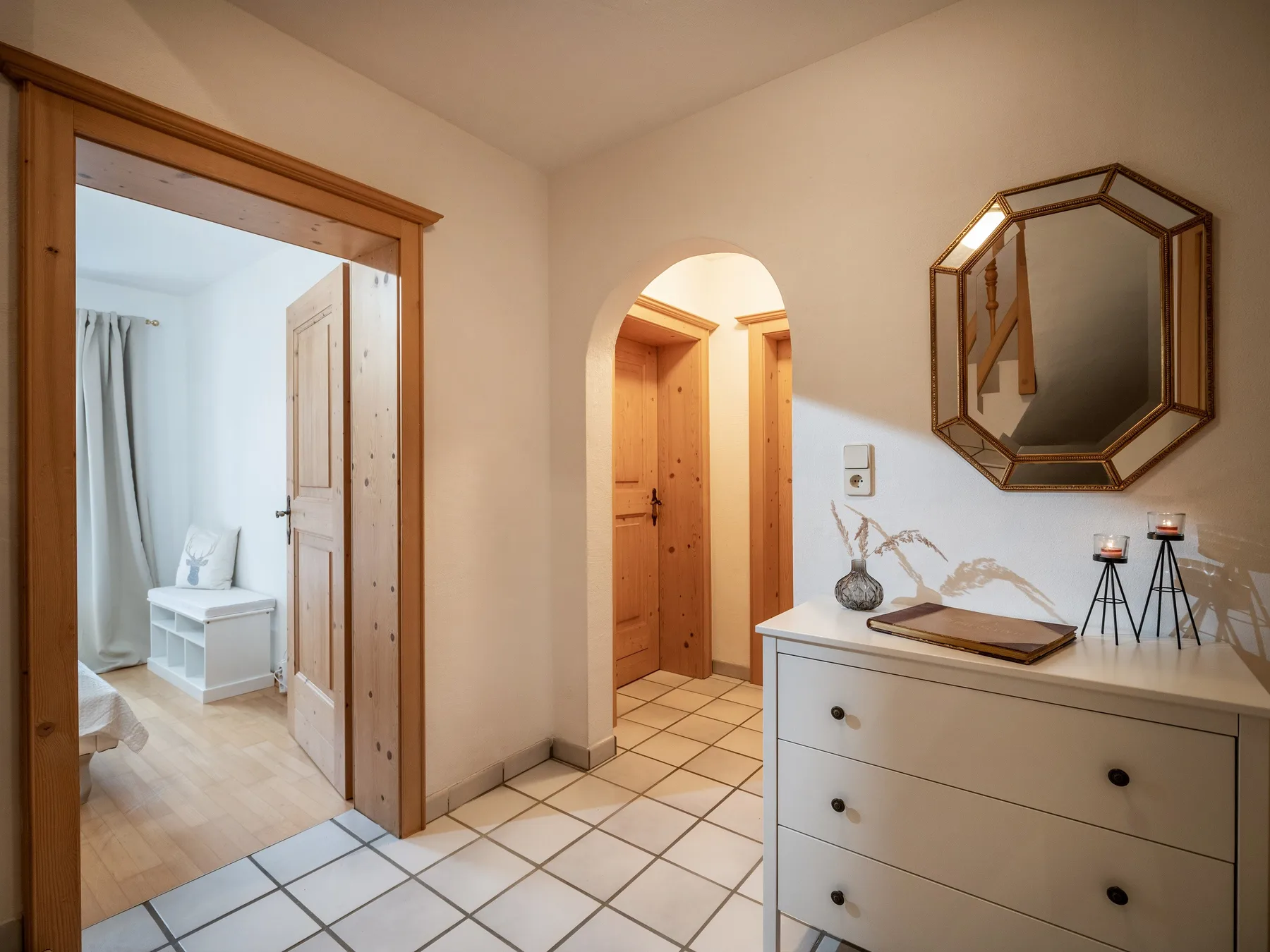 La entrada de un apartamento con una puerta abierta y una cómoda bajo un espejo.