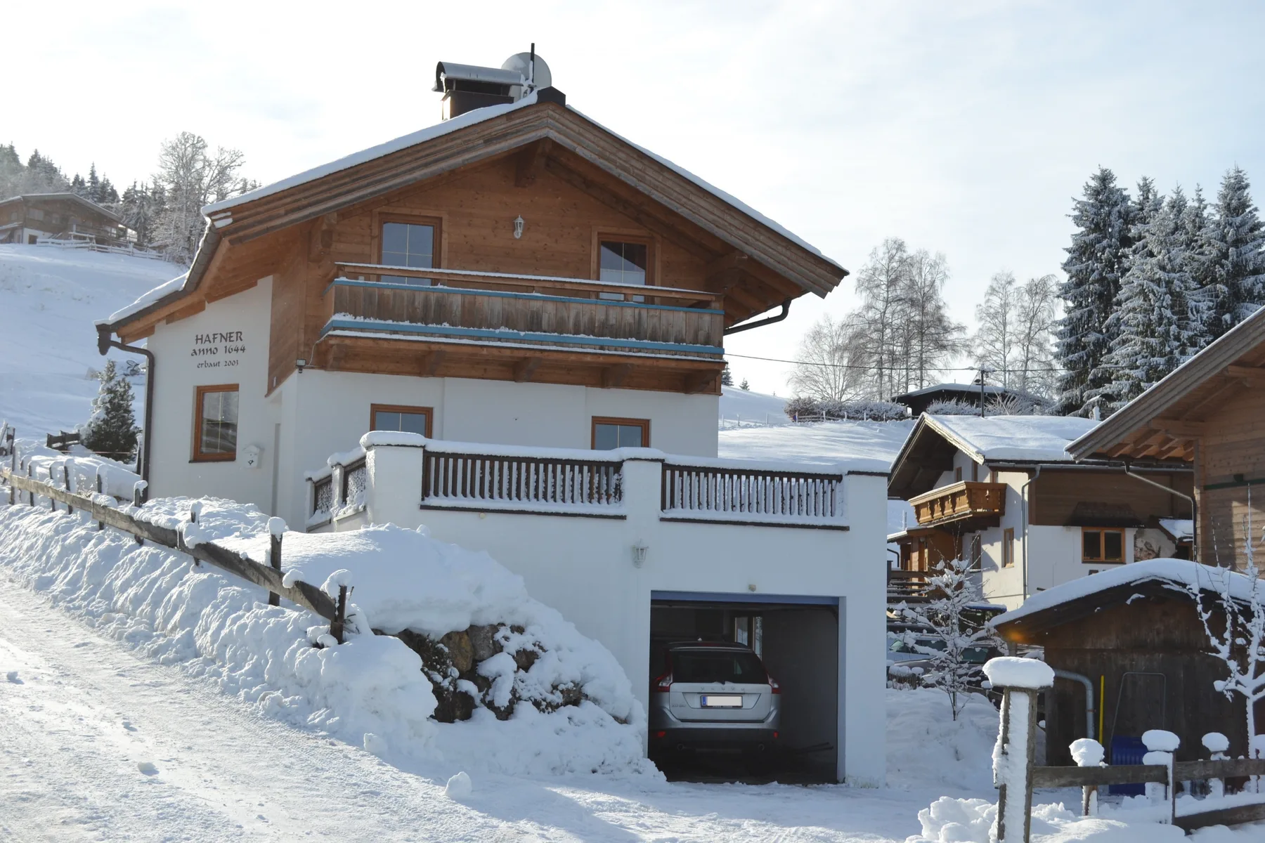 A chalet stands beside a snowy slope, with a car parked in the garage.