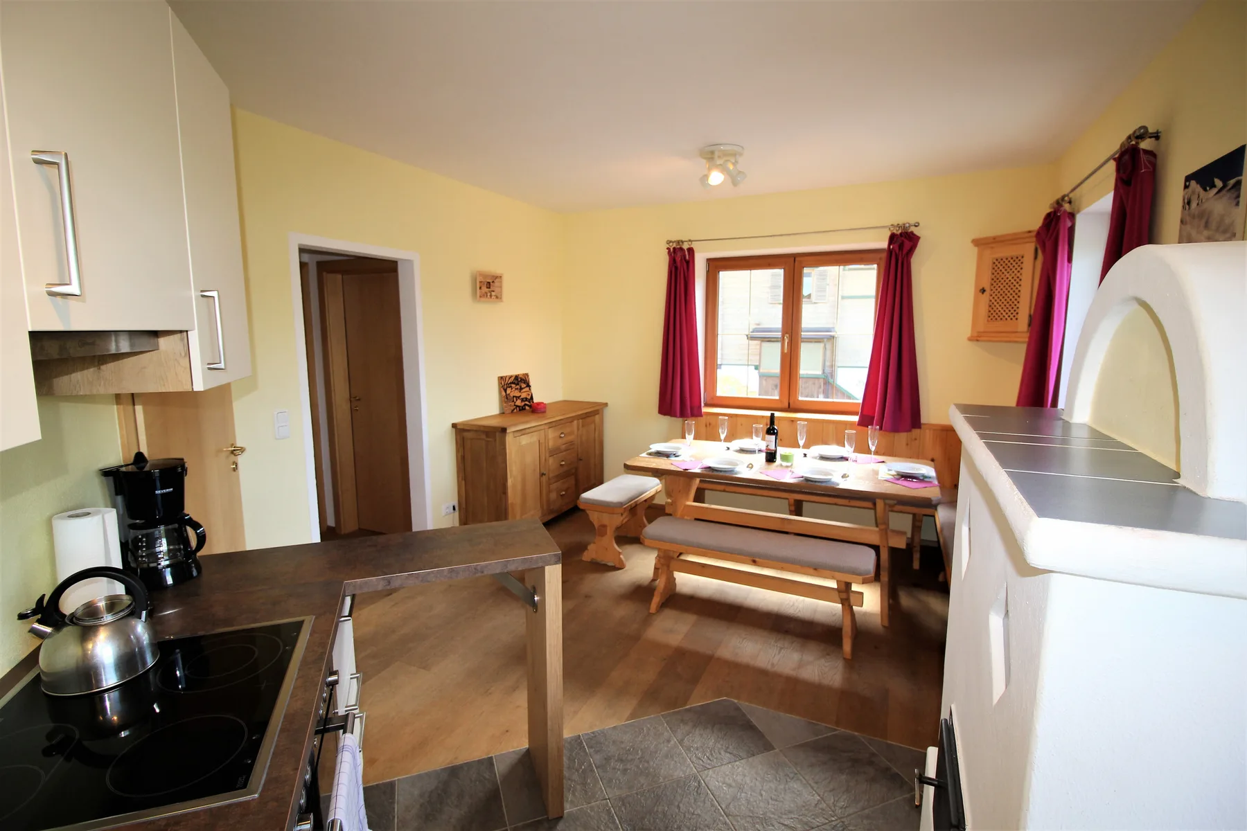 A kitchen and dining area with a table and red curtains.