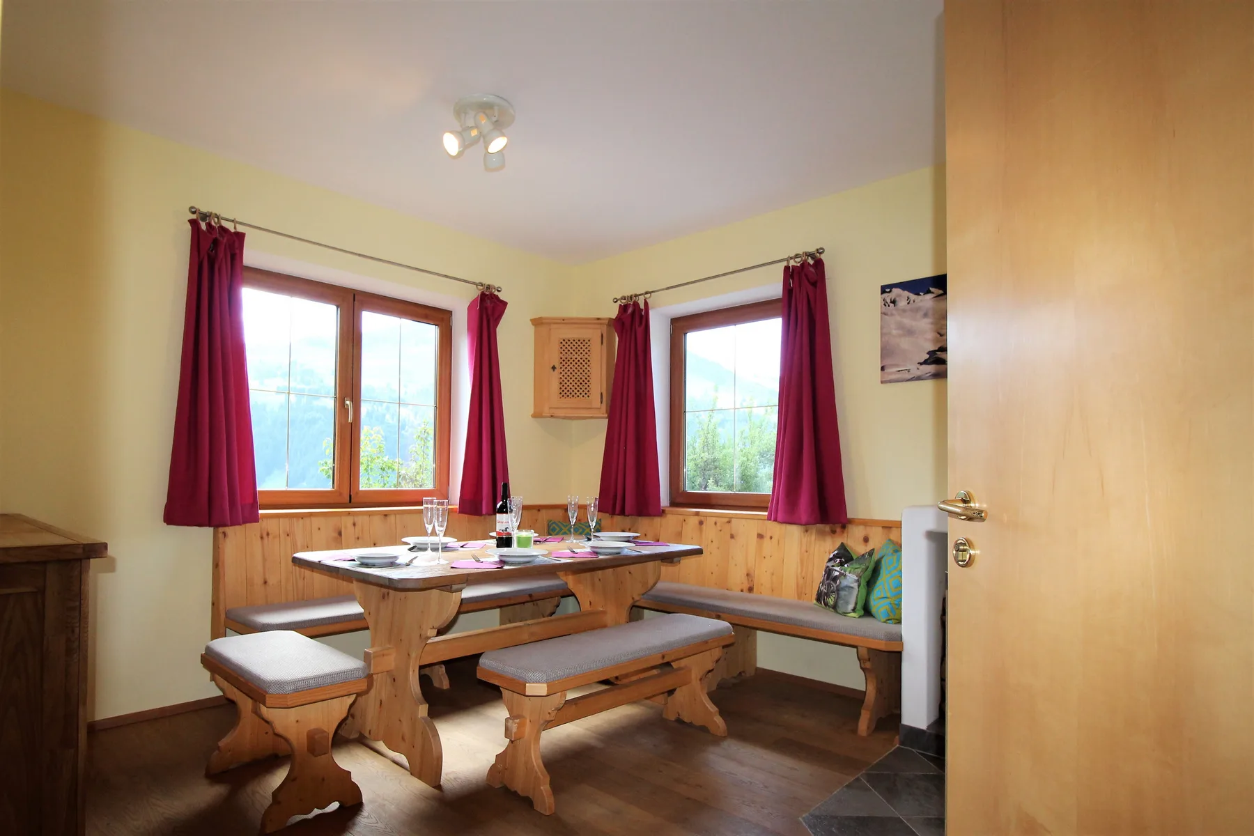A dining area with a wooden table and benches beside curtained windows.