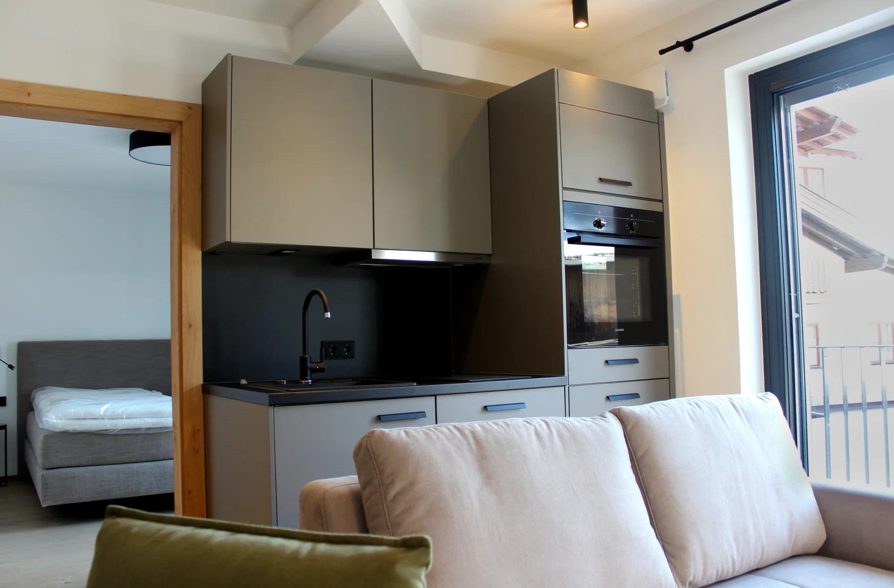 Una cocina moderna con un sofá en primer plano y un dormitorio visible a través de la puerta.