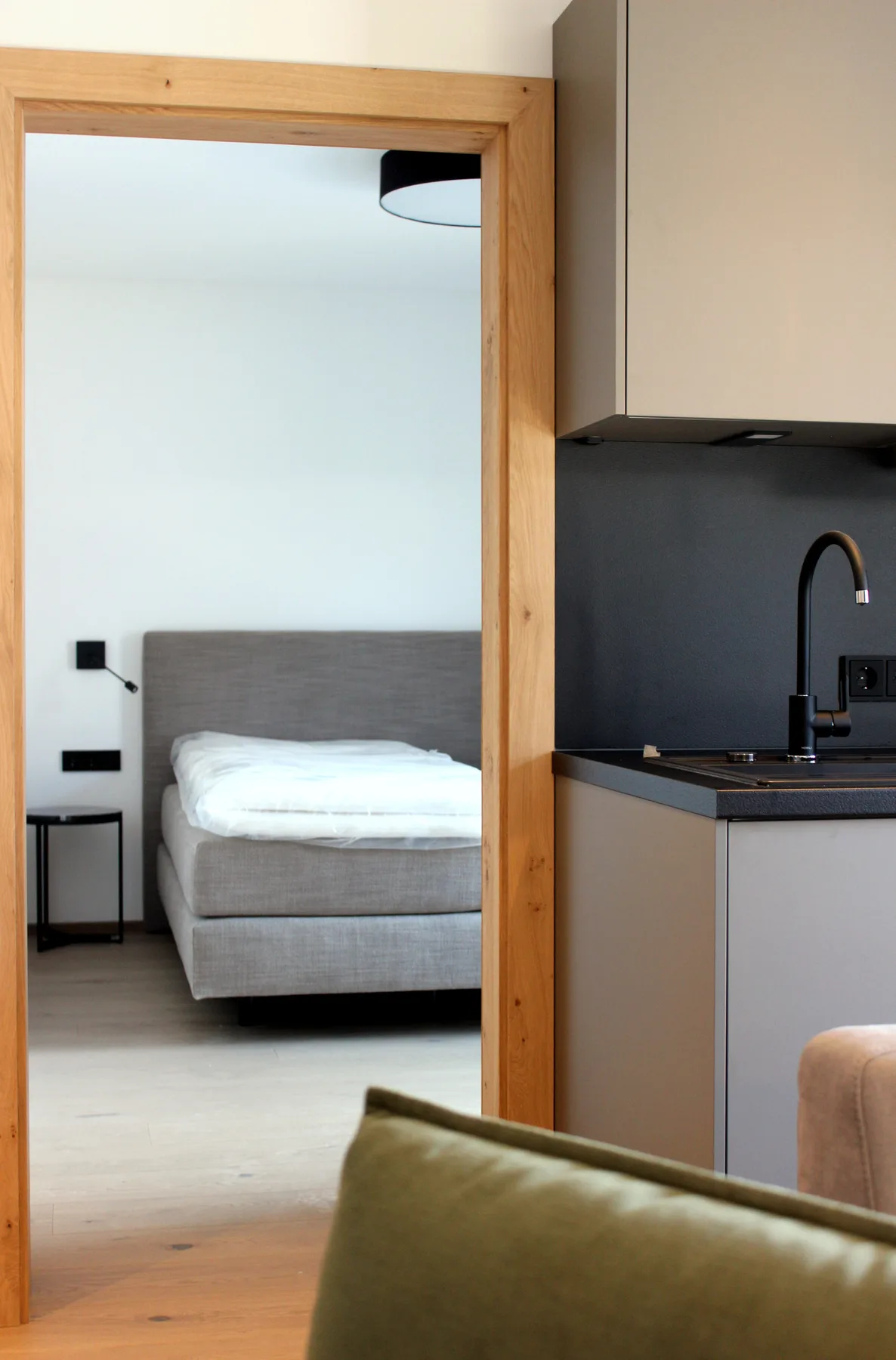Un dormitorio con la cama hecha se ve a través de una puerta de madera junto a la cocina.
