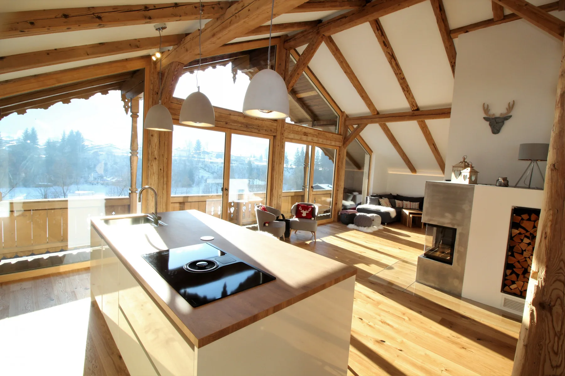 A bright open-plan living area with a kitchen island, fireplace, and large windows.