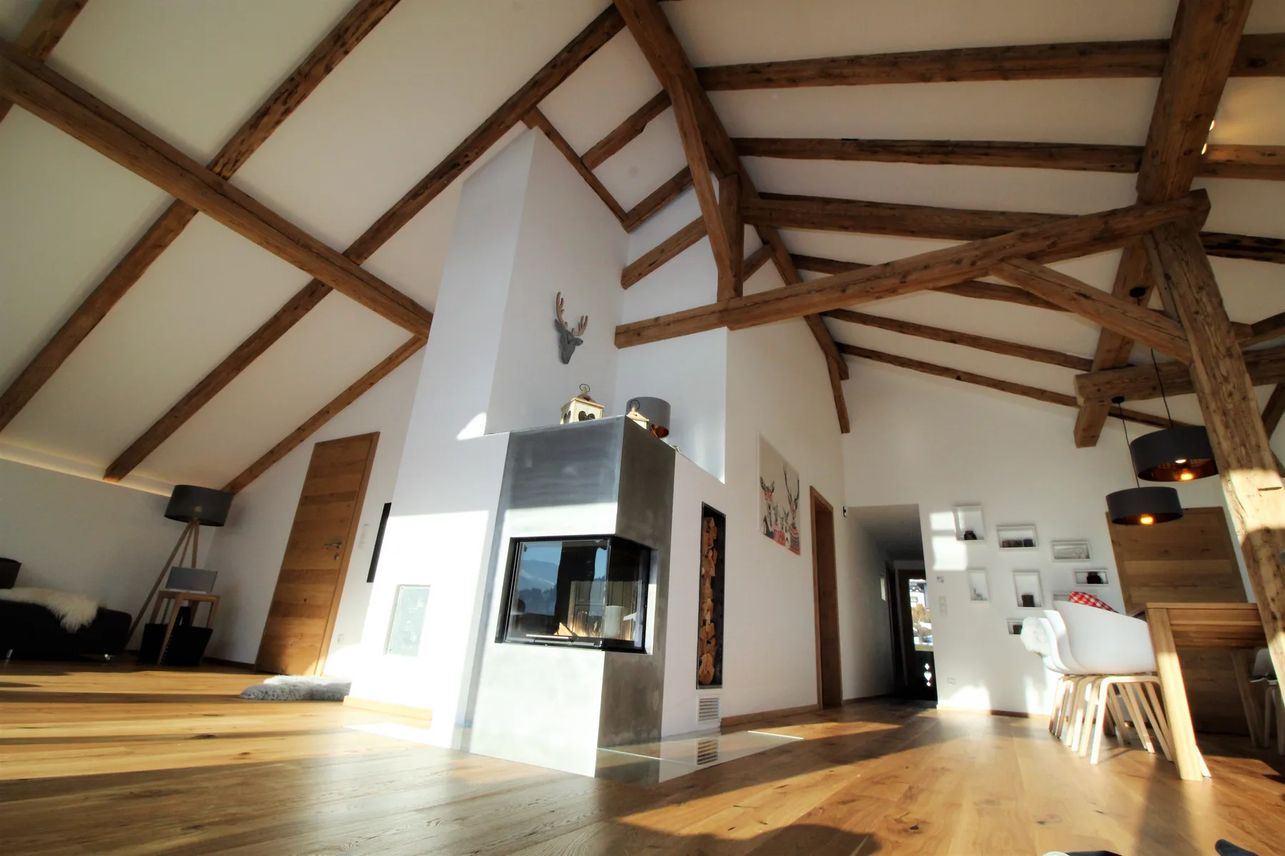 An open-plan living area with exposed wooden beams and a central fireplace.