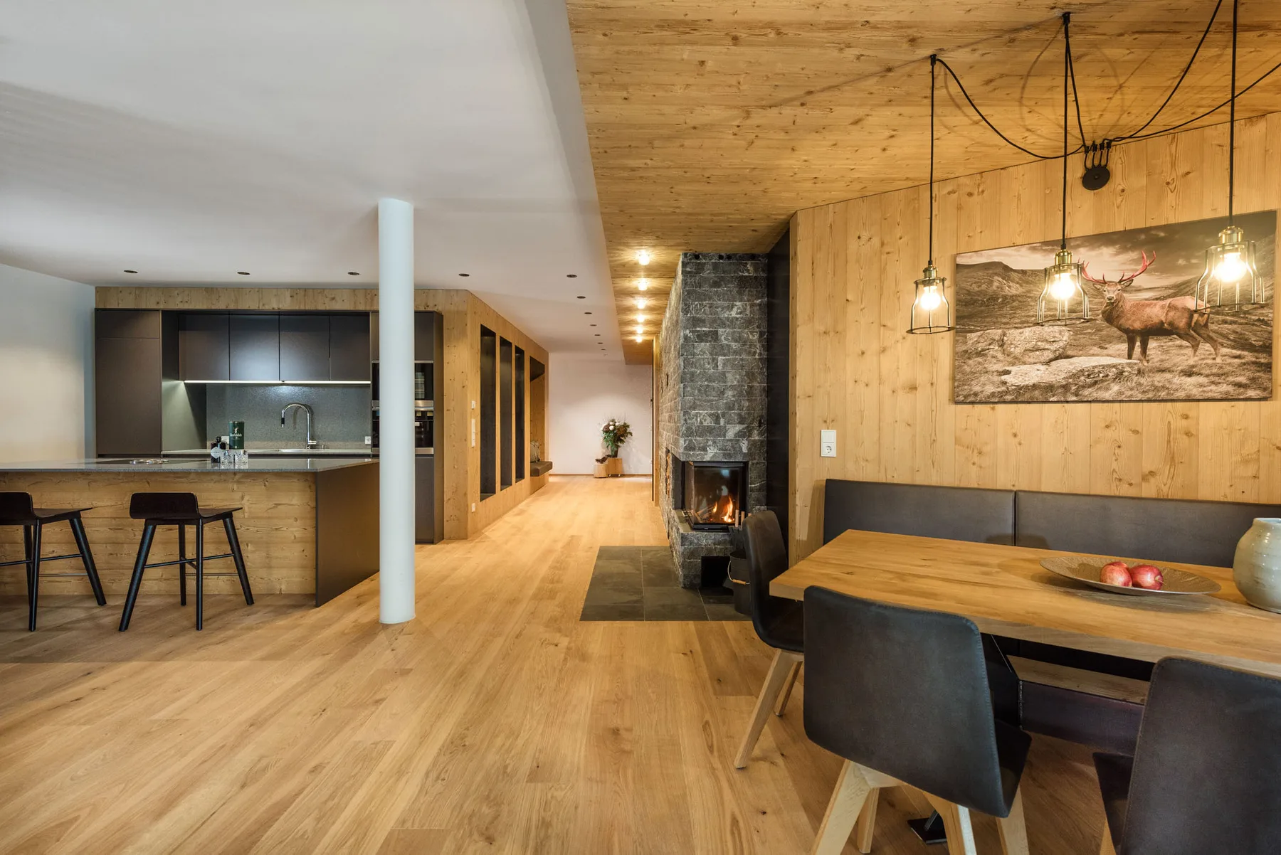 An open-plan kitchen and dining area with a long wooden table beside a fireplace.
