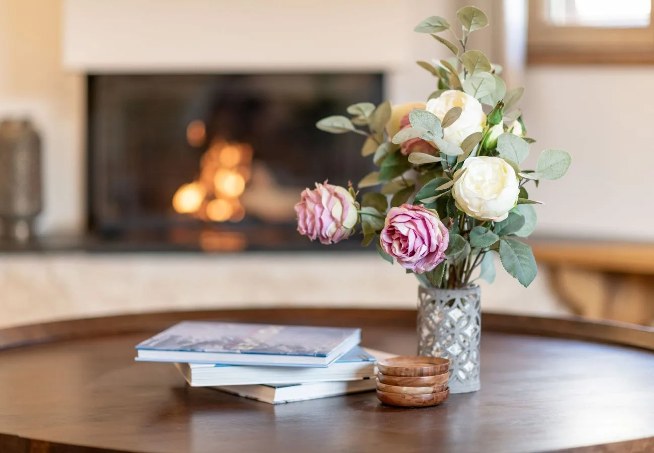 Una chimenea de sala se ve detrás de una mesa con flores y libros.