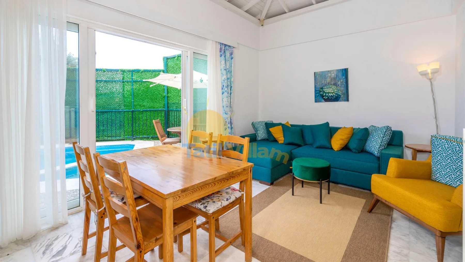 Una sala luminosa con asientos color turquesa y una mesa de comedor de madera junto a puertas de vidrio.