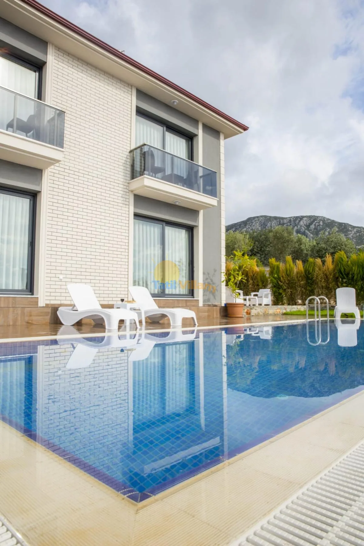 A modern house stands beside a swimming pool with white loungers.