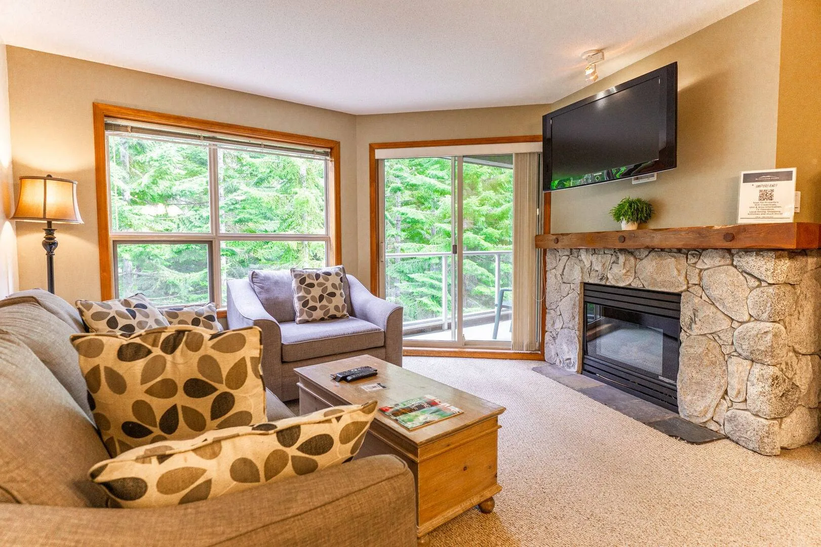 A living room with seating, large windows, and a stone fireplace.