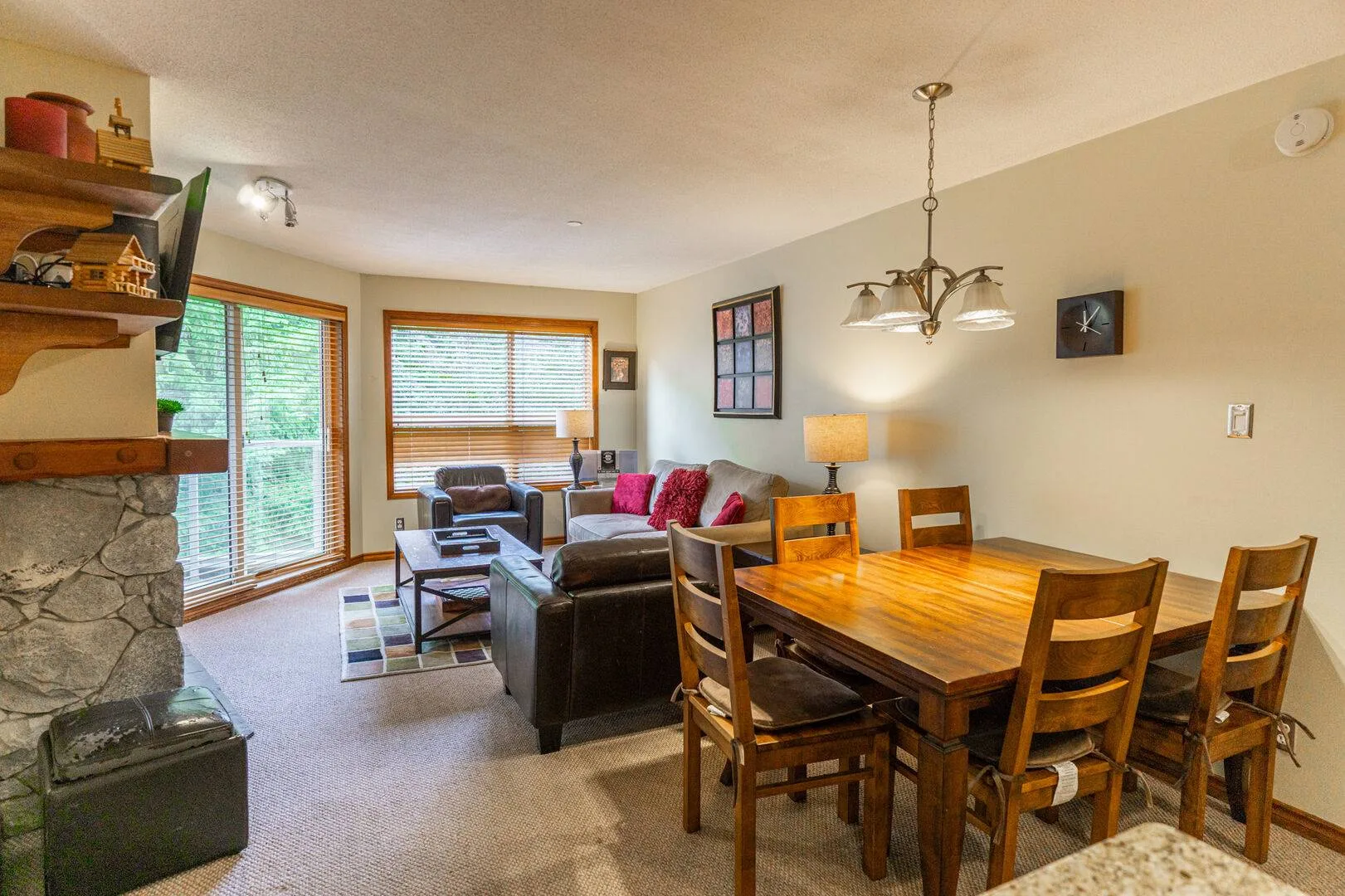 A living and dining area with a wooden table and seating beside large windows.