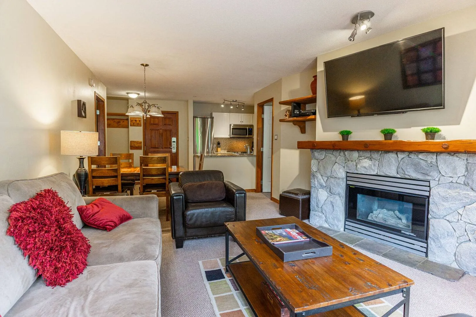 A living room with seating, a wooden coffee table, and a fireplace beneath a wall-mounted television.