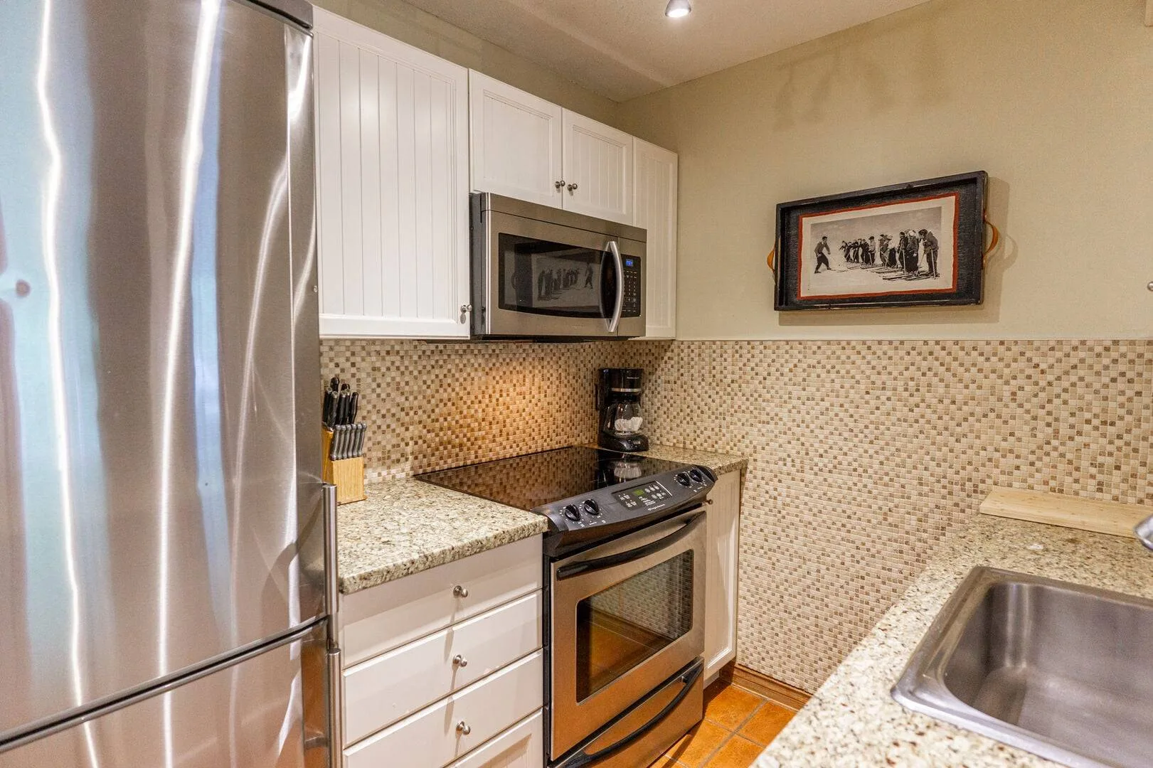 A kitchen with stainless steel appliances, white cabinetry, and speckled countertops.